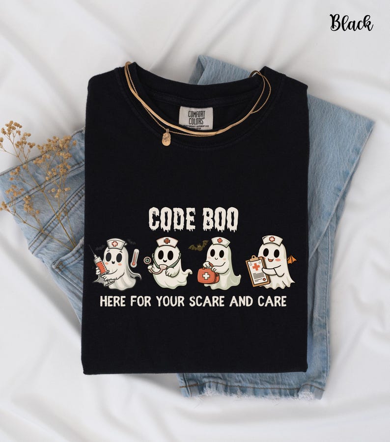 May include: Black t-shirt with the text "CODE BOO" and four cartoon ghost characters dressed as medical professionals. The ghosts hold a syringe, stethoscope, first aid kit, and clipboard. The phrase "HERE FOR YOUR SCARE AND CARE" is below the ghosts.