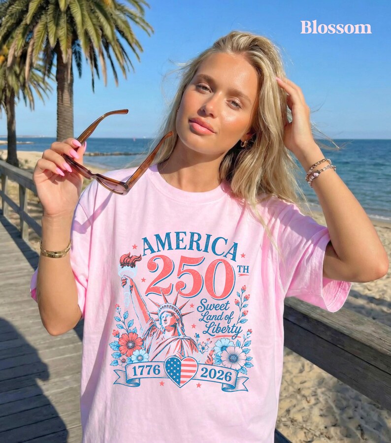 K&ouml;nnte beinhalten: Hellrosa T-Shirt mit dem Text "AMERICA 250TH Sweet Land of Liberty 1776-2026" und einer Grafik der Freiheitsstatue. Die Person tr&auml;gt eine Sonnenbrille.