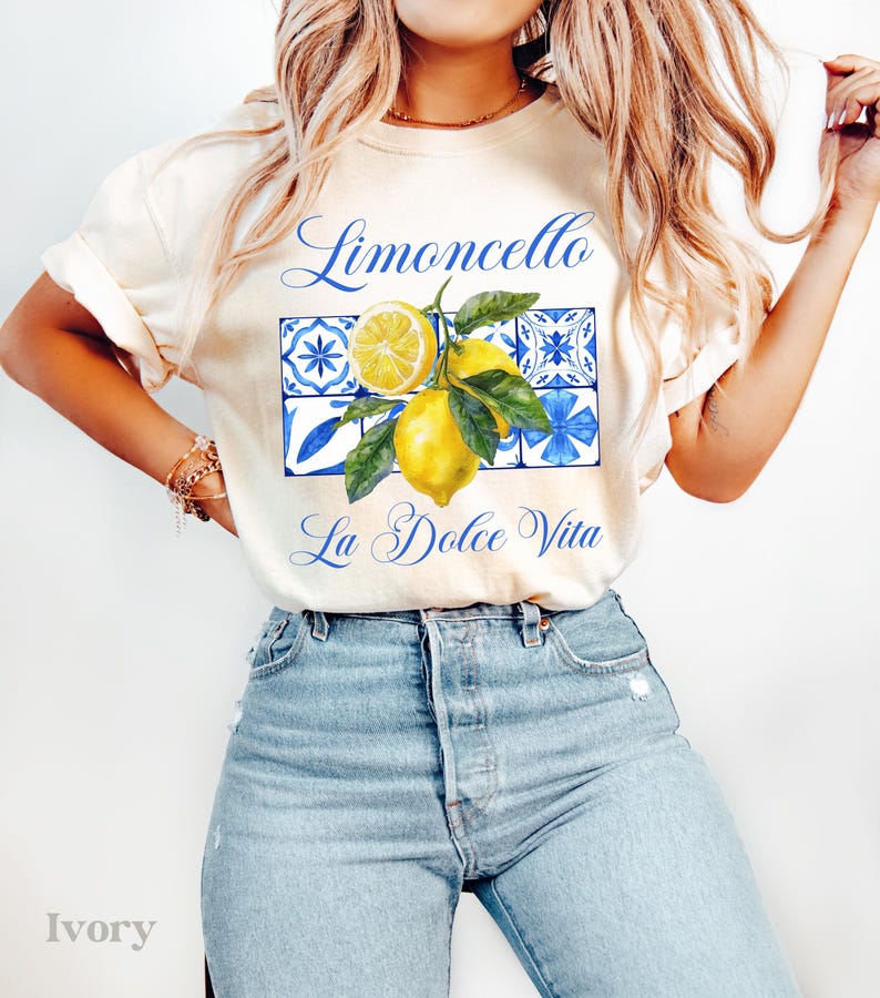 Pu&ograve; includere: Una maglietta bianca con il testo "Limoncello La Dolce Vita" e una grafica di limoni e piastrelle blu e bianche.