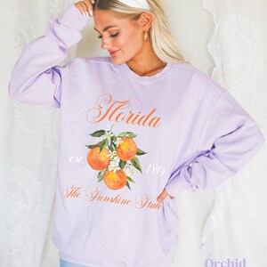 Florida sweatshirt that has a floral orange design saying Florida The Sunshine State est. 1845 on a summer crewneck Comfort Colors sweatshirt in the color orchid purple