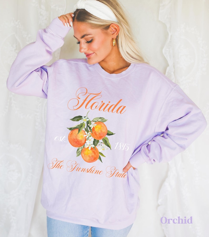 Florida sweatshirt that has a floral orange design saying Florida The Sunshine State est. 1845 on a summer crewneck Comfort Colors sweatshirt in the color orchid purple