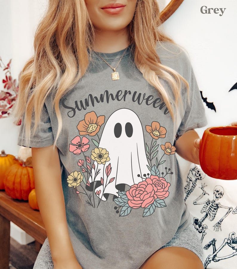 May include: Grey t-shirt with the word "Summerween" above a white ghost illustration surrounded by colorful flowers. The ghost has two black oval eyes. The flowers are in shades of pink, yellow, and orange.