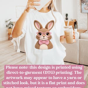 May include: White t-shirt featuring a cartoon bunny wearing pink glasses and a bow tie. The bunny has a knitted appearance. The text on the image states that the design is printed using direct-to-garment printing.