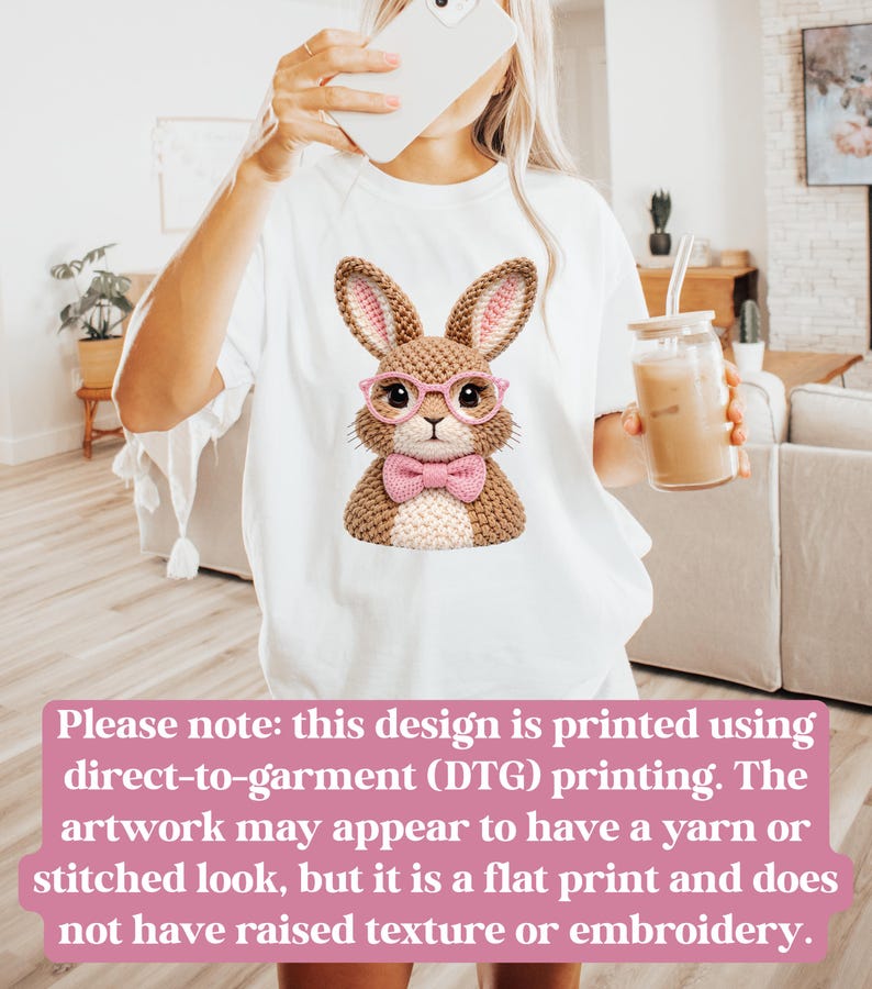 May include: White t-shirt featuring a cartoon bunny wearing pink glasses and a bow tie. The bunny has a knitted appearance. The text on the image states that the design is printed using direct-to-garment printing.