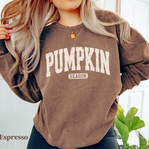 Puede incluir: Sudadera color espresso con el texto "PUMPKIN SEASON" en blanco, con una fuente de estilo universitario. La sudadera tiene cuello redondo y mangas largas. El estilo general es informal y c&oacute;modo.
