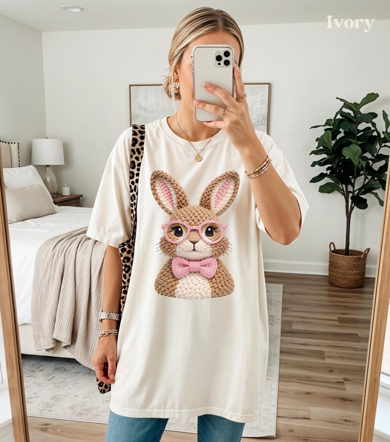 May include: Ivory-colored t-shirt featuring a detailed graphic of a bunny wearing pink glasses and a bow tie. The bunny has brown and pink accents. The shirt is a relaxed fit, suitable for casual wear.