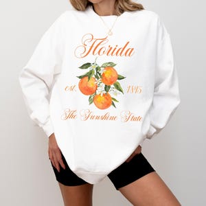 Florida sweatshirt that has a floral orange design saying Florida The Sunshine State est. 1845 on a summer crewneck Comfort Colors sweatshirt in the color white