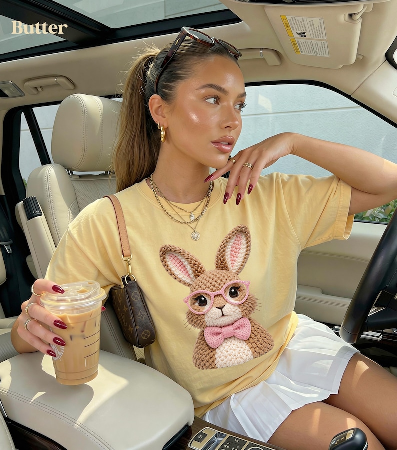 May include: A light yellow t-shirt featuring a detailed illustration of a bunny wearing pink glasses and a bow tie. The bunny has brown and pink crochet details. The word "Butter" is in the top left corner.