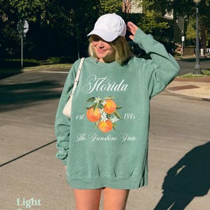 Florida sweatshirt that has a floral orange design saying Florida The Sunshine State est. 1845 on a summer crewneck Comfort Colors sweatshirt in the color light green