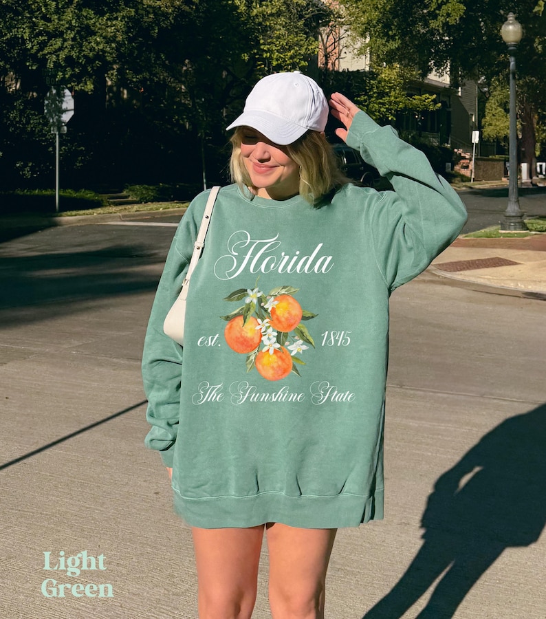 Florida sweatshirt that has a floral orange design saying Florida The Sunshine State est. 1845 on a summer crewneck Comfort Colors sweatshirt in the color light green