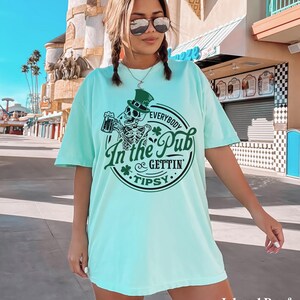 skeleton pub crawl shirt for your St. Patrick's Day party that has a skeleton holding a beer wearing a green Leprechaun hat with shamrocks saying Everybody in the Pub Gettin' Tipsy on a Comfort Colors shirt in the color island reef