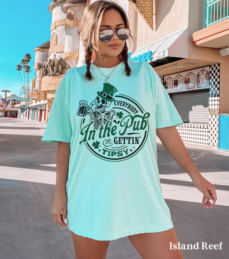skeleton pub crawl shirt for your St. Patrick's Day party that has a skeleton holding a beer wearing a green Leprechaun hat with shamrocks saying Everybody in the Pub Gettin' Tipsy on a Comfort Colors shirt in the color island reef