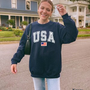 Pu&ograve; includere: Felpa blu navy con una grafica bianca "USA" e una piccola bandiera americana.