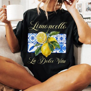 Pu&ograve; includere: Maglietta nera con una grafica di limone e il testo "Limoncello La Dolce Vita" in un font bianco corsivo.