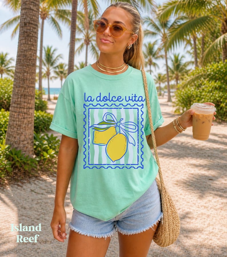 Pu&ograve; includere: T-shirt verde chiaro con la scritta "la dolce vita" e una grafica di due limoni gialli legati con un nastro blu. La maglietta ha una vestibilit&agrave; comoda.