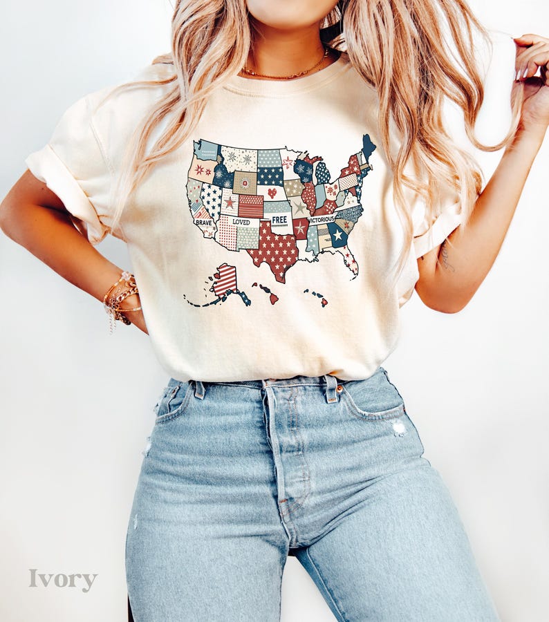 May include: A white t-shirt with a patchwork design of the United States map. The map is made up of red, white, and blue squares with stars and the words "Brave", "Loved", "Free", and "Victorious" printed on it.