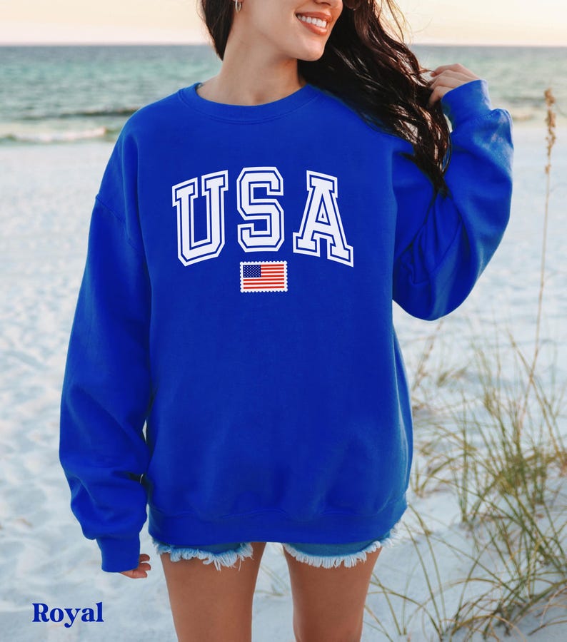Pu&ograve; includere: Una felpa blu reale con la scritta "USA" in bianco con un contorno bianco e un piccolo grafico della bandiera americana sotto.