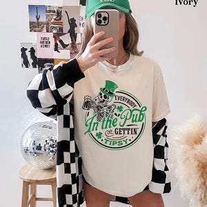 skeleton pub crawl shirt for your St. Patrick's Day party that has a skeleton holding a beer wearing a green Leprechaun hat with shamrocks saying Everybody in the Pub Gettin' Tipsy on a Comfort Colors shirt in the color ivory