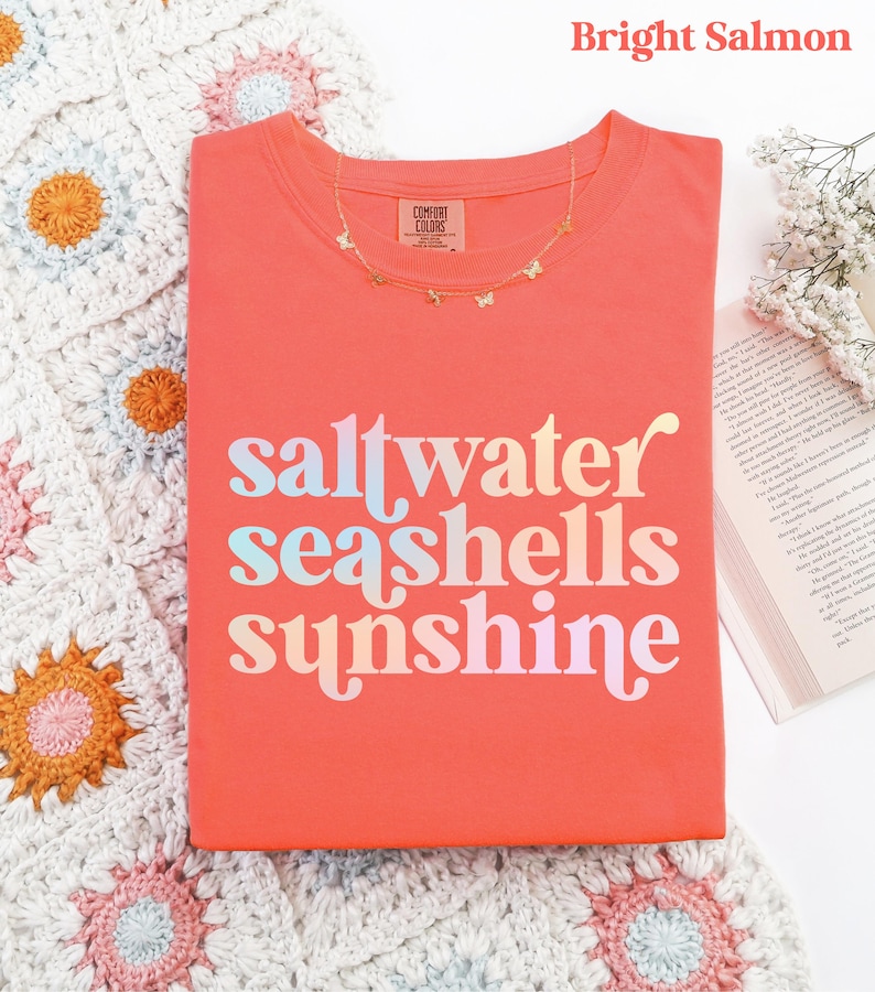 sunshine beach vacation shirt that says saltwater seashells sunshine in a fun summer print on a Comfort Colors shirt in the color bright salmon orange