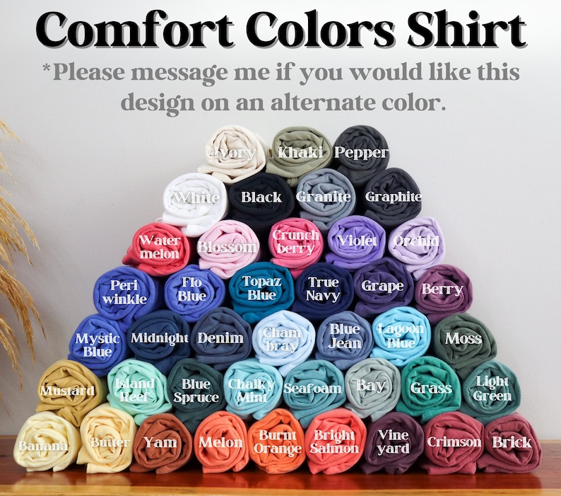 May include: Rolled Comfort Colors shirts in a variety of colours, such as white, black, and blue, are displayed. The text at the top reads "Comfort Colors Shirt." Further text encourages enquiries about alternative colours.