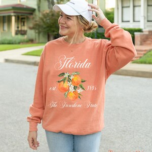 Florida sweatshirt that has a floral orange design saying Florida The Sunshine State est. 1845 on a summer crewneck Comfort Colors sweatshirt in the color terracotta orange