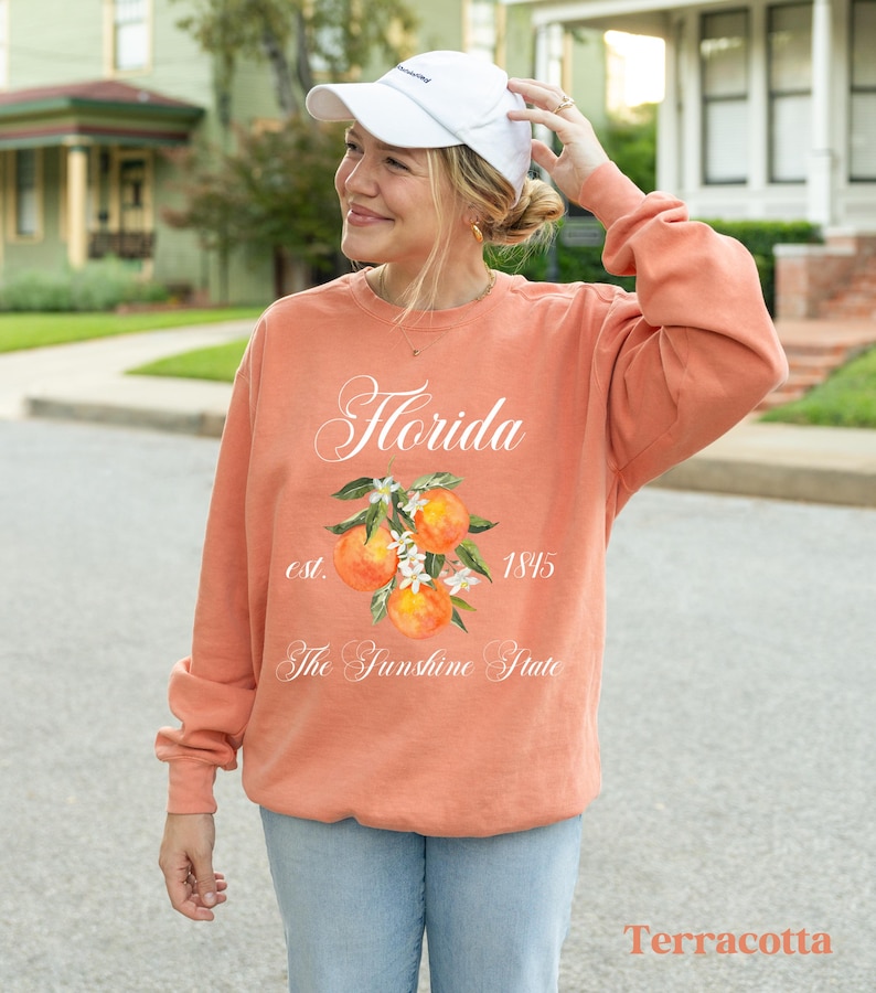 Florida sweatshirt that has a floral orange design saying Florida The Sunshine State est. 1845 on a summer crewneck Comfort Colors sweatshirt in the color terracotta orange