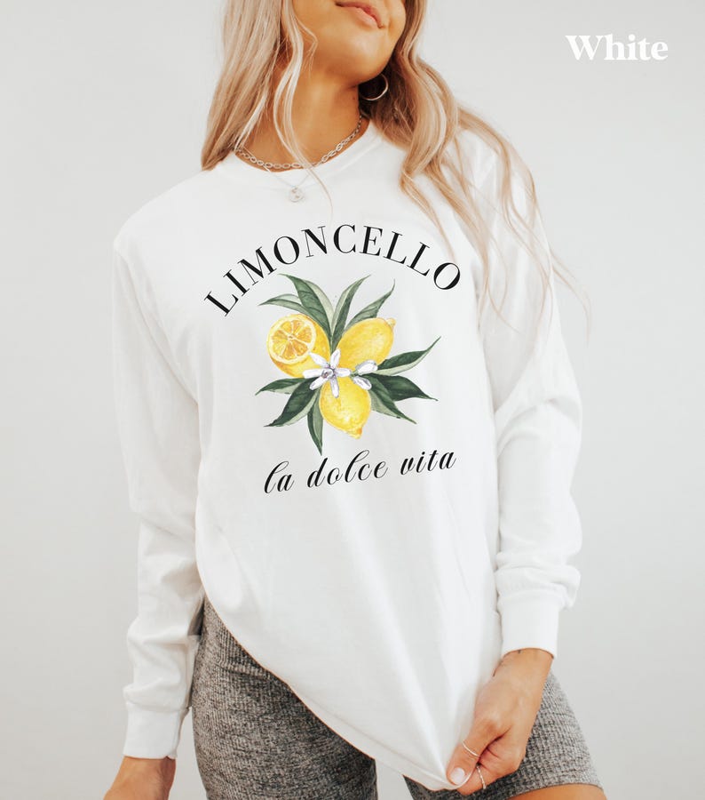 May include: White long-sleeve shirt with a watercolor design featuring lemons, leaves, and the text "Limoncello" and "la dolce vita". The shirt is a casual style, perfect for everyday wear.