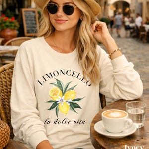 May include: Ivory-colored sweatshirt with the word "LIMONCELLO" above a lemon and leaf graphic, and the phrase "la dolce vita" below. The sweatshirt is long-sleeved and has a crew neck.