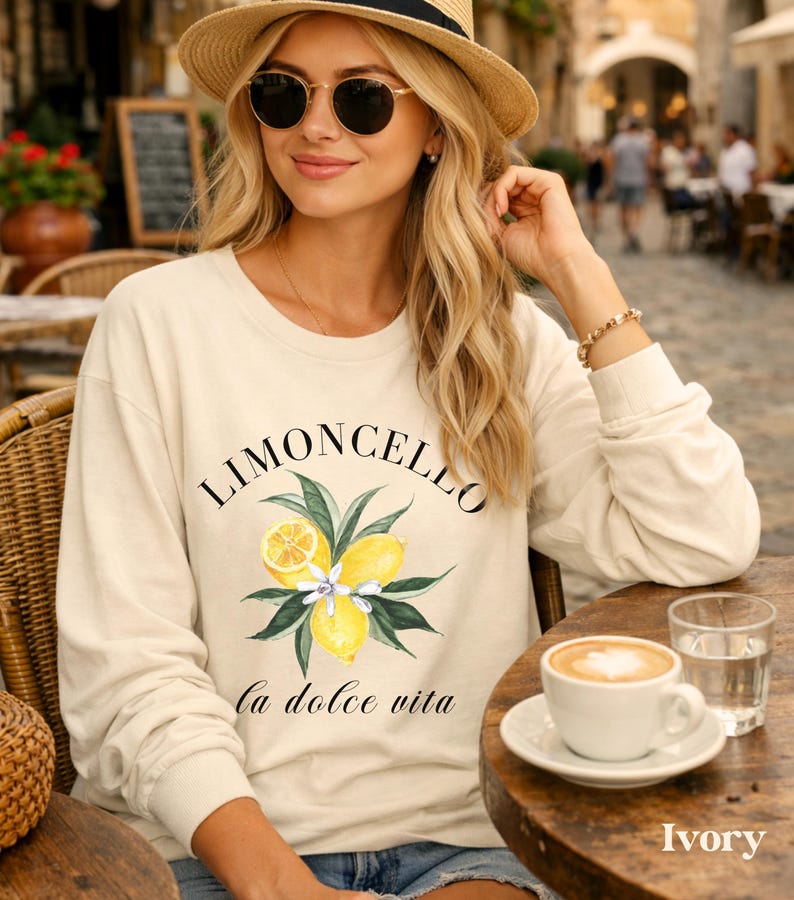 May include: Ivory-colored sweatshirt with the word "LIMONCELLO" above a lemon and leaf graphic, and the phrase "la dolce vita" below. The sweatshirt is long-sleeved and has a crew neck.