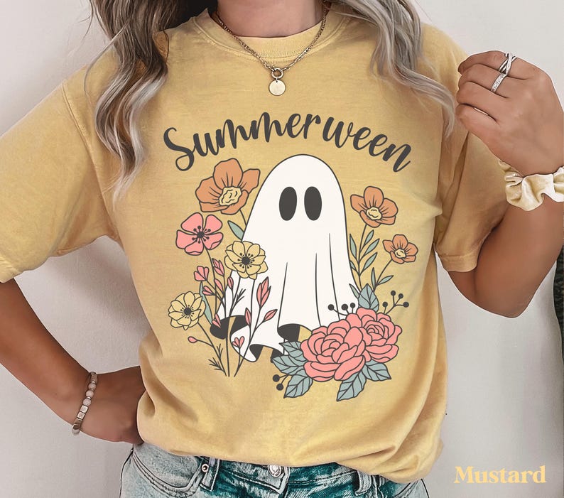 May include: Mustard-colored t-shirt with the word "Summerween" above a cartoon ghost surrounded by flowers. The ghost has two black oval eyes and is draped in a white sheet. The flowers are in shades of pink, orange, and yellow.