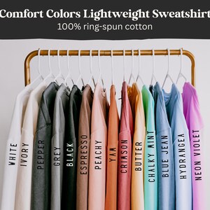 Puede incluir: Una exhibici&oacute;n de sudaderas ligeras Comfort Colors en varios colores, incluyendo blanco, marfil, pimienta, gris, negro, espresso, melocot&oacute;n, &ntilde;ame, carmes&iacute;, mantequilla, menta tiza, vaquero azul, hortensia y ne&oacute;n violeta. El texto dice "Comfort Colors Lightweight Sweatshirt" y "100% ring-spun cotton".