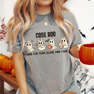 nurse Halloween Comfort Colors shirt that has 4 spooky nurses reading Code Boo: here for your scare and care for er nurse or nightshift nurse in the color grey