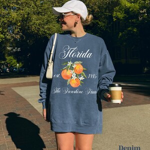 Florida sweatshirt that has a floral orange design saying Florida The Sunshine State est. 1845 on a summer crewneck Comfort Colors sweatshirt in the color denim blue