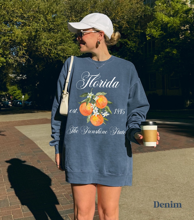 Florida sweatshirt that has a floral orange design saying Florida The Sunshine State est. 1845 on a summer crewneck Comfort Colors sweatshirt in the color denim blue