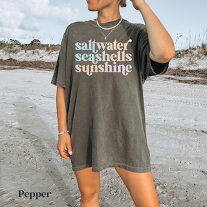 sunshine beach vacation shirt that says saltwater seashells sunshine in a fun summer print on a Comfort Colors shirt in the color pepper
