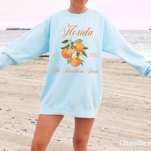 Florida sweatshirt that has a floral orange design saying Florida The Sunshine State est. 1845 on a summer crewneck Comfort Colors sweatshirt in the color chambray light blue