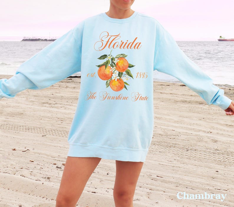 Florida sweatshirt that has a floral orange design saying Florida The Sunshine State est. 1845 on a summer crewneck Comfort Colors sweatshirt in the color chambray light blue