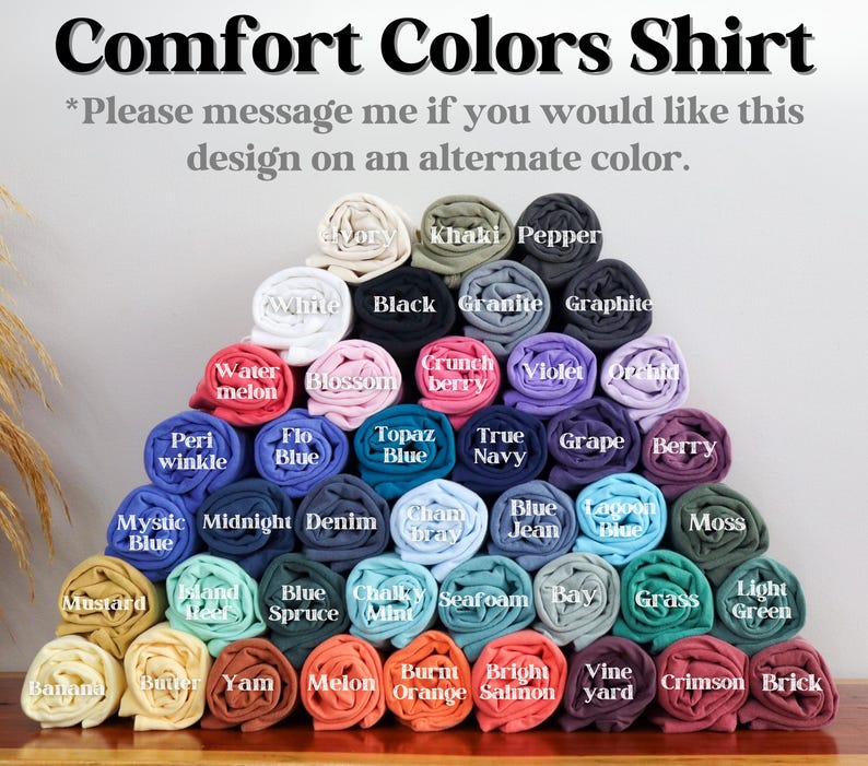 May include: A display of rolled Comfort Colors shirts in various colors, including white, black, and blue. The text at the top reads "Comfort Colors Shirt." Additional text encourages inquiries about alternate colors.
