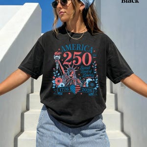 K&ouml;nnte beinhalten: Schwarzes T-Shirt mit einer Grafik zum 250. Jahrestag Amerikas. Das Design zeigt die Freiheitsstatue, die Jahre 1776 und 2026 sowie den Text "America 250th Sweet Land of Liberty."