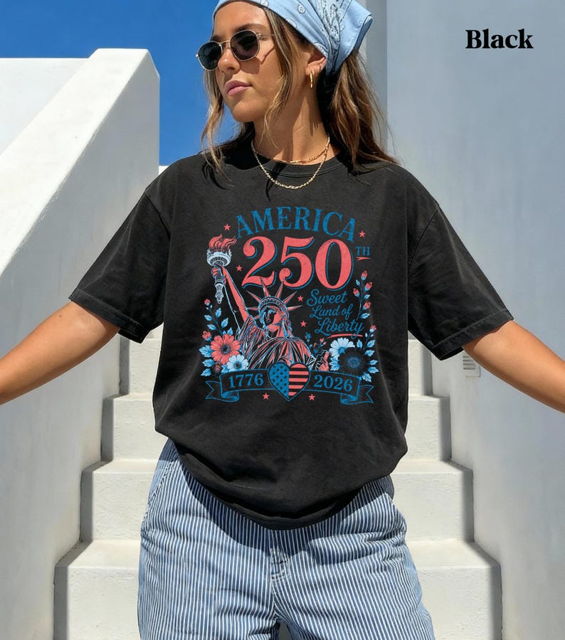 K&ouml;nnte beinhalten: Schwarzes T-Shirt mit einer Grafik zum 250. Jahrestag Amerikas. Das Design zeigt die Freiheitsstatue, die Jahre 1776 und 2026 sowie den Text "America 250th Sweet Land of Liberty."