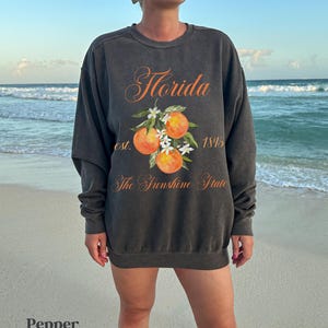 Florida sweatshirt that has a floral orange design saying Florida The Sunshine State est. 1845 on a summer crewneck Comfort Colors sweatshirt in the color pepper