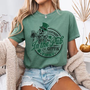 skeleton pub crawl shirt for your St. Patrick's Day party that has a skeleton holding a beer wearing a green Leprechaun hat with shamrocks saying Everybody in the Pub Gettin' Tipsy on a Comfort Colors shirt in the color light green