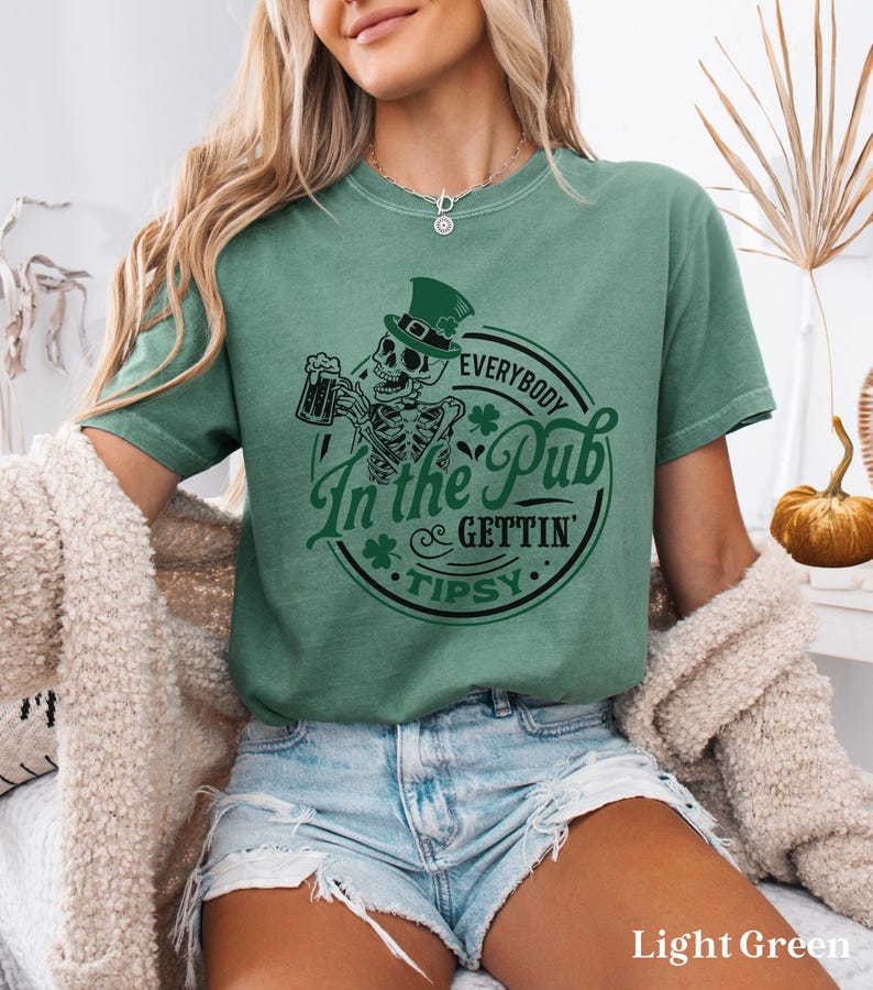 skeleton pub crawl shirt for your St. Patrick's Day party that has a skeleton holding a beer wearing a green Leprechaun hat with shamrocks saying Everybody in the Pub Gettin' Tipsy on a Comfort Colors shirt in the color light green
