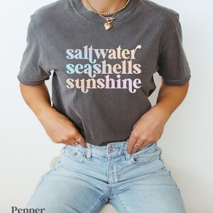 sunshine beach vacation shirt that says saltwater seashells sunshine in a fun summer print on a Comfort Colors shirt in the color pepper