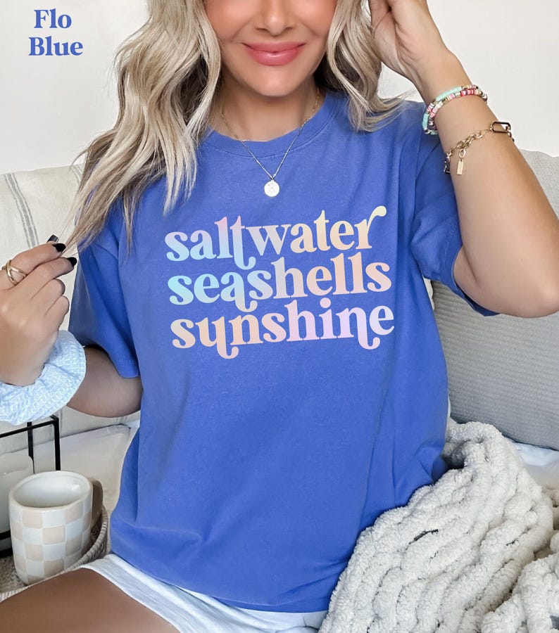 sunshine beach vacation shirt that says saltwater seashells sunshine in a fun summer print on a Comfort Colors shirt in the color flo blue