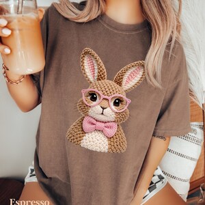 May include: Espresso-colored t-shirt featuring a crocheted bunny wearing pink glasses and a bow tie. The bunny has brown and white fur with pink inner ears. The word "Espresso" is printed at the bottom of the shirt.