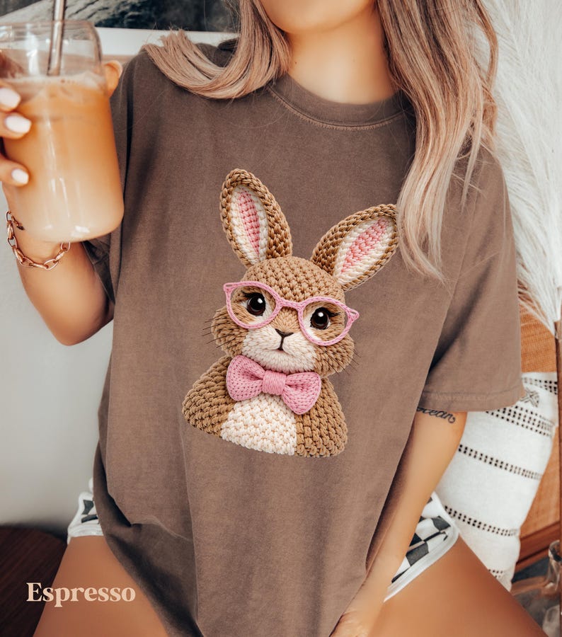 May include: Espresso-colored t-shirt featuring a crocheted bunny wearing pink glasses and a bow tie. The bunny has brown and white fur with pink inner ears. The word "Espresso" is printed at the bottom of the shirt.