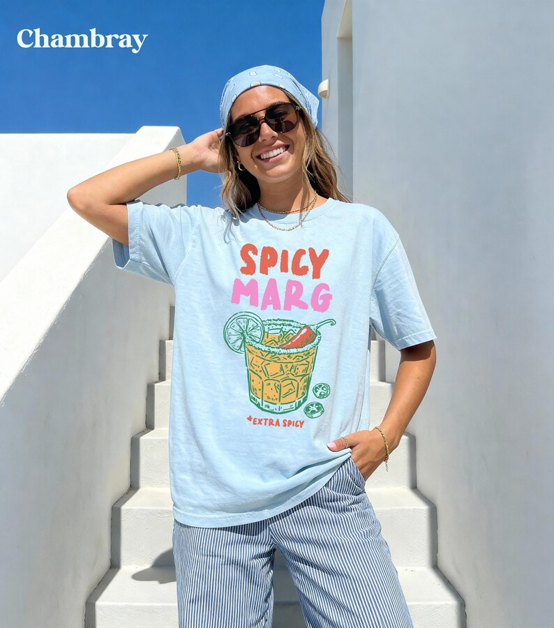 Puede incluir: Camiseta azul claro con la frase "Spicy Marg" en rojo y rosa, y un gr&aacute;fico de c&oacute;ctel con lima y chile. La camiseta tambi&eacute;n tiene las palabras "Extra Spicy" debajo del c&oacute;ctel.
