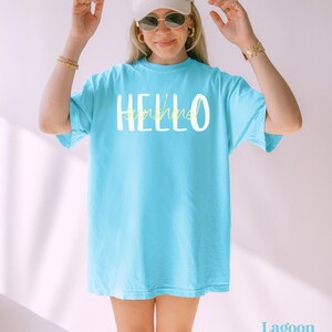 May include: A turquoise t-shirt with the words "HELLO sunshine" printed on the front in white and yellow. The shirt has a loose fit and short sleeves. The colour is Lagoon Blue.