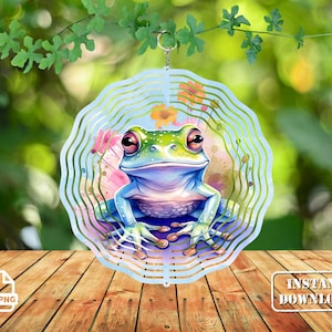 May include: A blue and green frog wind spinner with a floral design. The frog is sitting on a flower with its legs outstretched. The wind spinner is made of metal and has a circular shape.